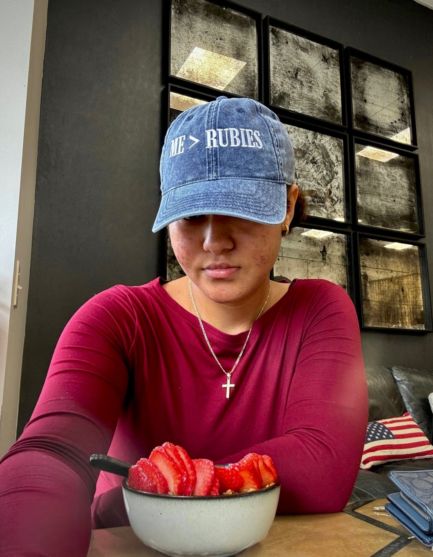 Person wearing a blue cap with text, sitting at a table with a bowl of fruit.