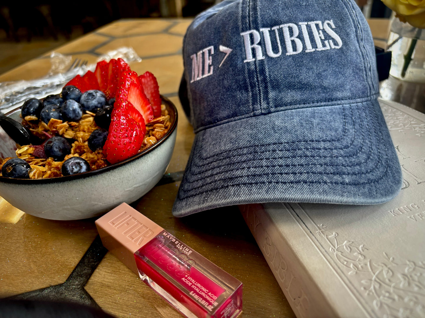 Blue cap next to a bowl of fruit and a box of makeup on a table.