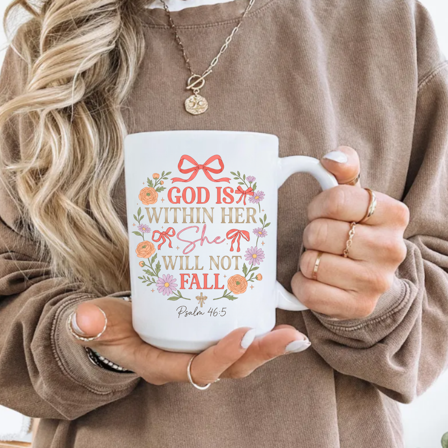 Person holding a mug with decorative text 'God is within her, she will not fall' and design