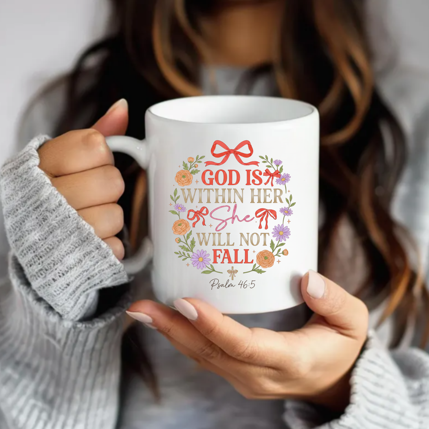 Person holding a mug with decorative text 'God is within her, she will not fall' and floral design