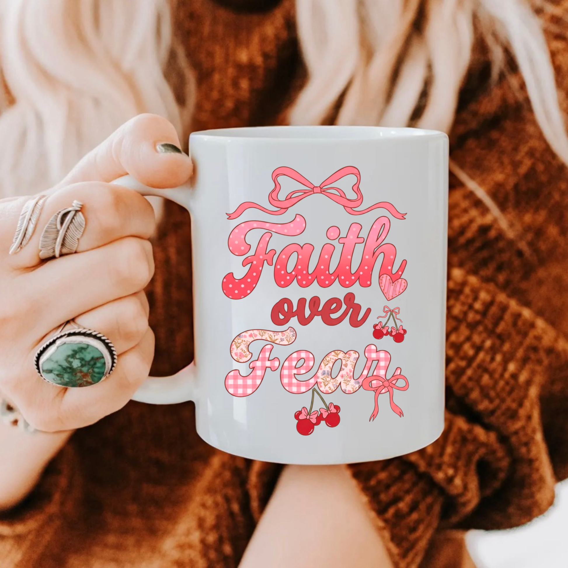 Person holding a mug with 'Faith over Fear' text in pink, wearing a brown sweater.