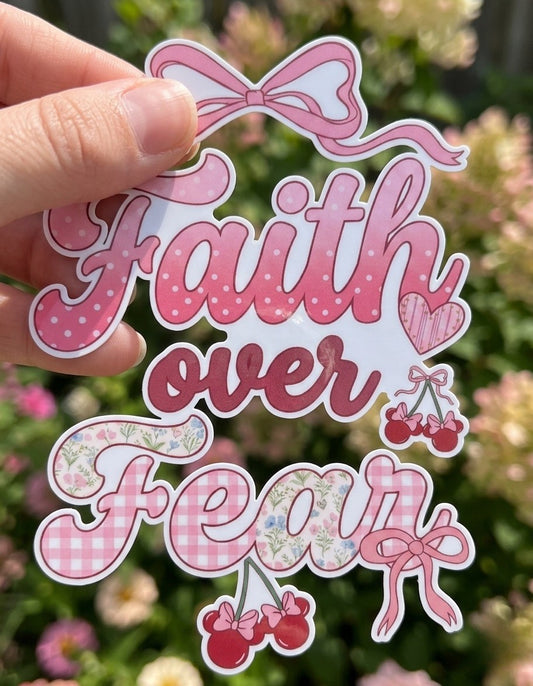 Pink 'Faith over Fear' sticker held by a hand with a floral background