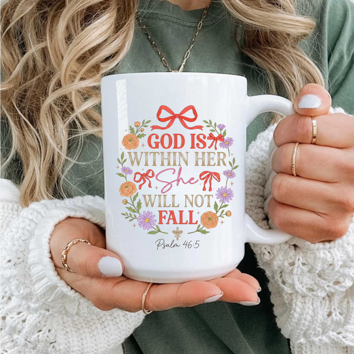 Person holding a white mug with decorative text 'God is within her, she will not fall' and design