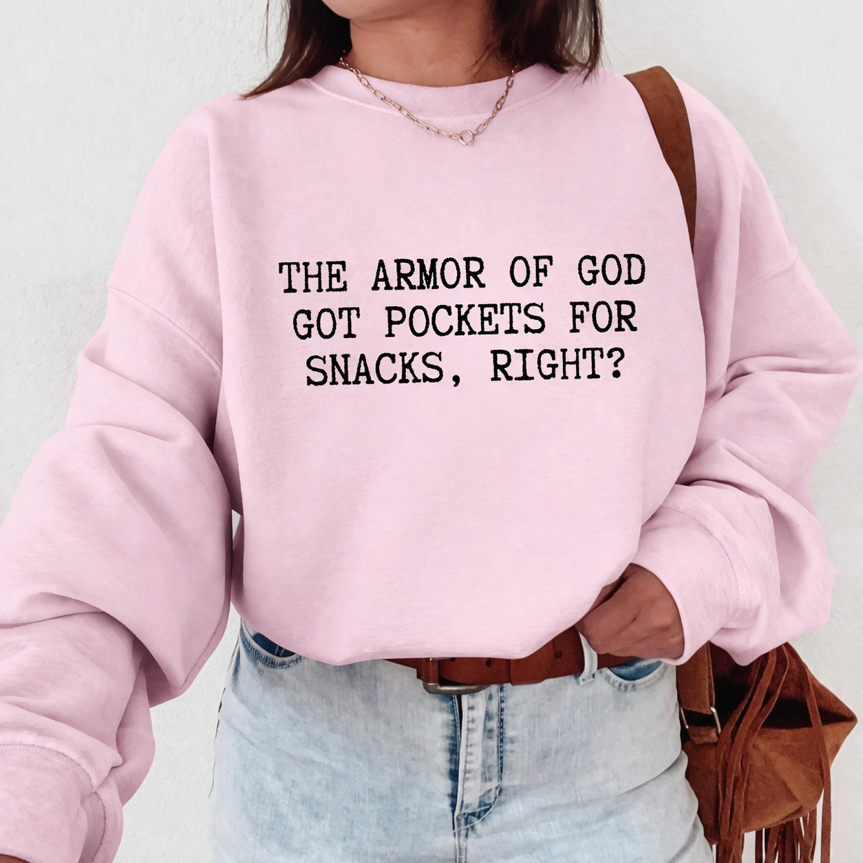 Person wearing a pink sweatshirt with text 'The Armor of God got pockets for snacks, right?', standing against a plain background