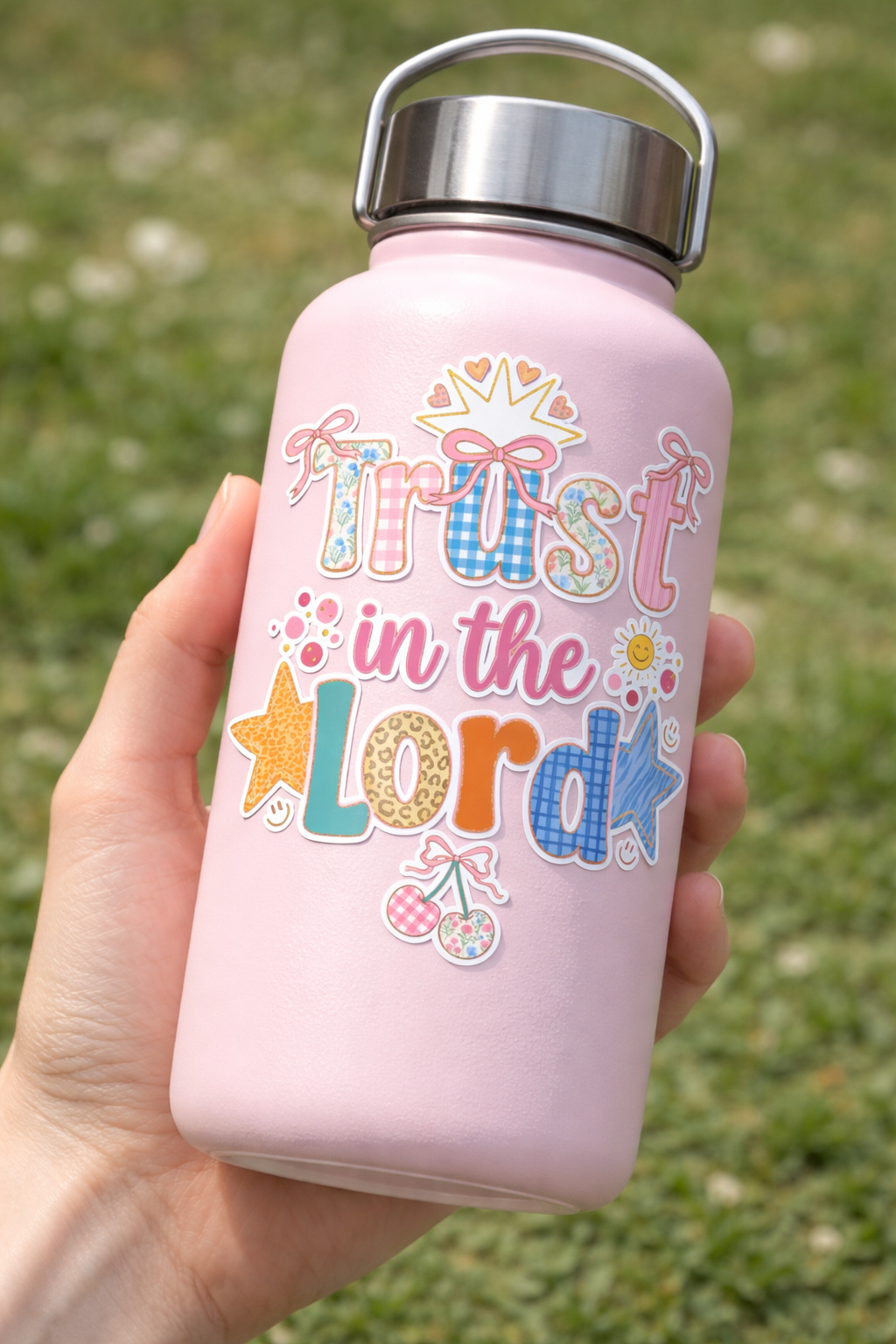 Pink water bottle with 'Trust in the Lord' sticker held in a hand against a grassy background