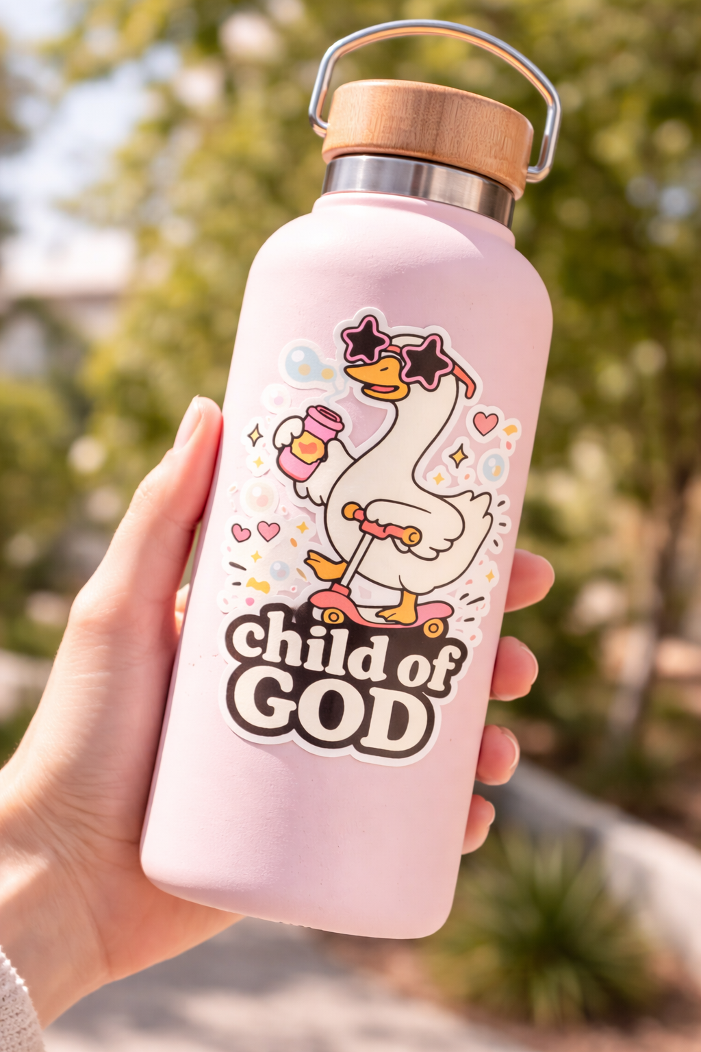 Pink water bottle with cartoon goose design and 'child of God' text, held outdoors.