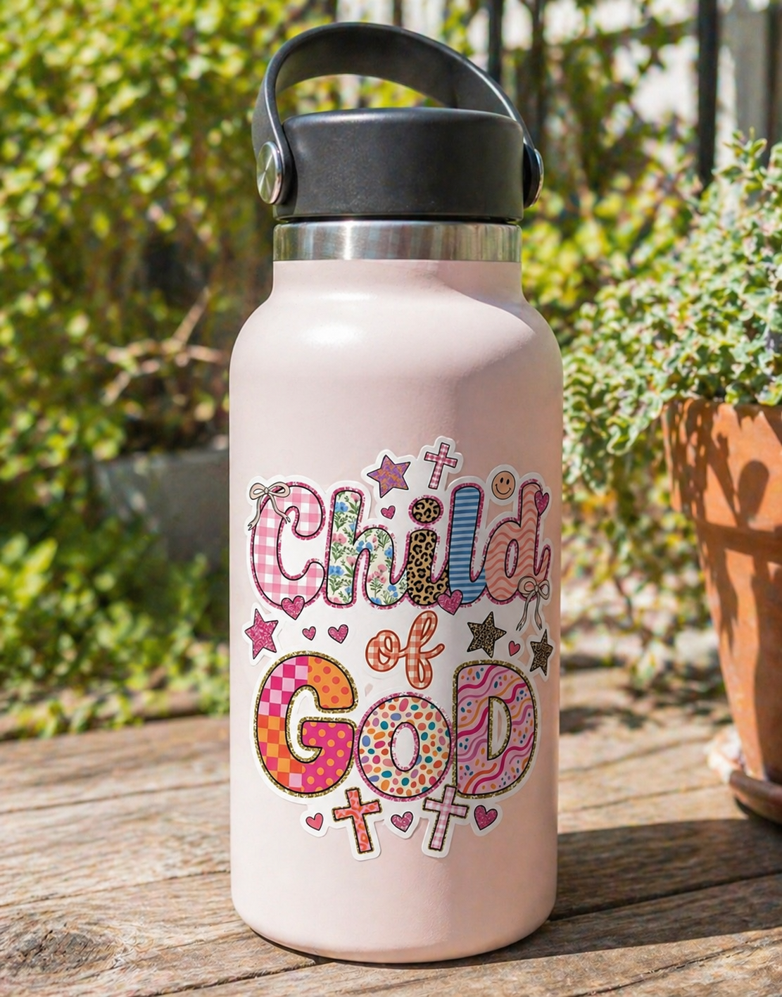 Child of God Christian sticker on a pink tumbler water bottle with colorful patchwork design, shown outdoors with a soft natural background.