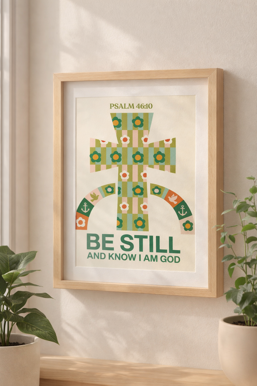 A light wood picture frame rests on a hardwood floor against a neutral wall, featuring a pastel floral cross illustration with “Psalm 46:10” and the phrase “Be still and know I am God,” styled in a calm, modern interior with soft daylight and subtle shadows.