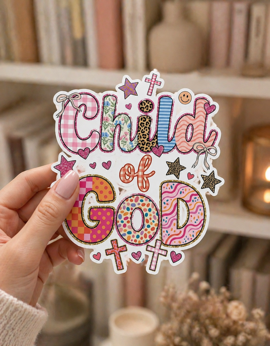 Hand holding a colorful child of God sticker with playful patchwork lettering in pink, blue, floral, and leopard print, surrounded by crosses, hearts, stars, and bows against a cozy blurred bookshelf background.