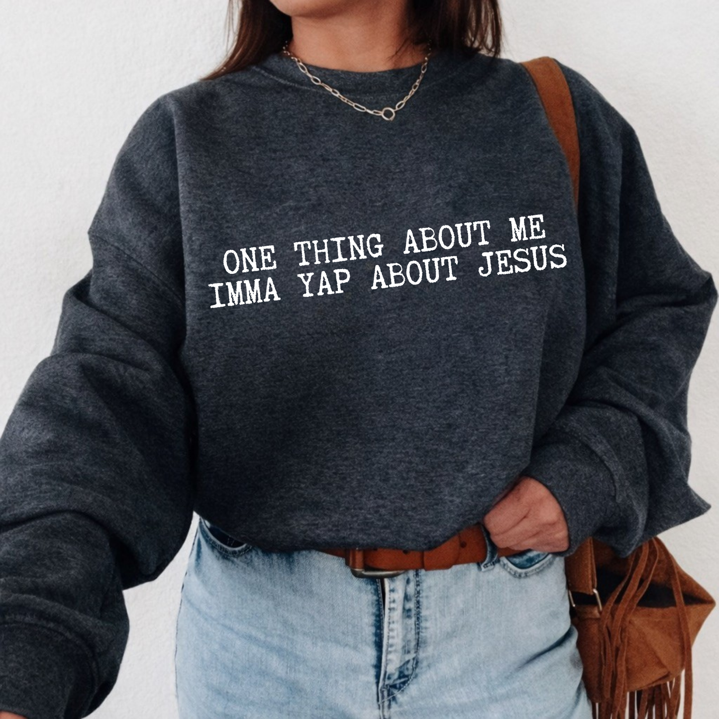 Person wearing a dark gray sweatshirt with text 'ONE THING ABOUT ME IMMA YAP ABOUT JESUS', standing against a plain background