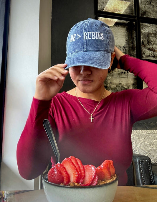 Person wearing a blue cap with text, sitting at a table with a bowl of fruit.