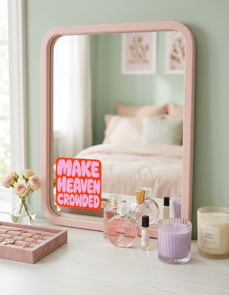 Pink mirror on a dresser with perfumes, candles, and a 'Make Heaven Crowded' sticker.