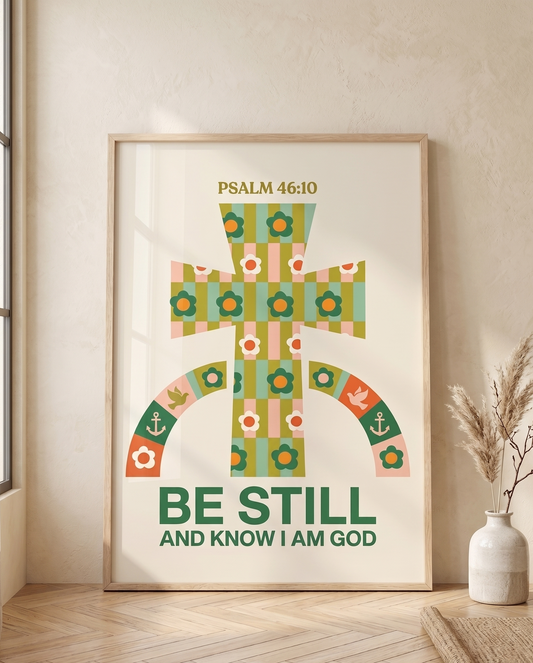 Framed Psalm 46:10 floral cross print leaning against a neutral wall on a light wood floor, styled with pampas grass and woven decor in soft natural light.