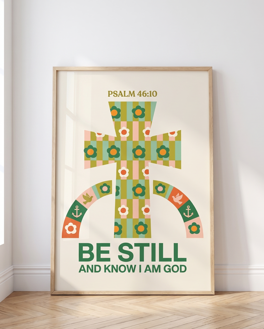 Scandinavian-style interior with an 11x14 wooden frame featuring a colorful Christian poster reading “Be Still and Know I Am God,” resting against the wall.