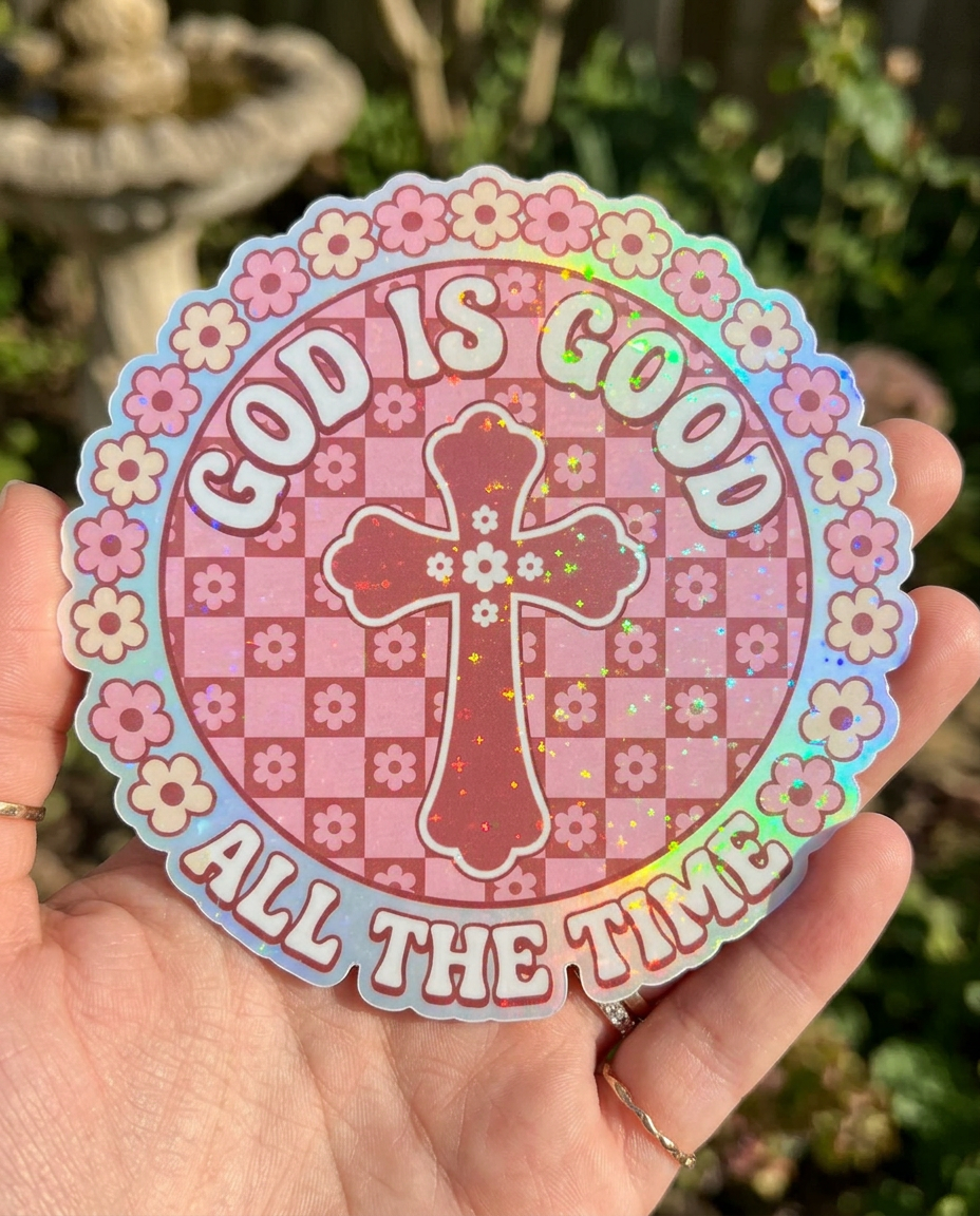 Holographic Christian sticker with pink floral checkerboard design featuring a decorative cross and the phrase “God Is Good All The Time” in retro bubble lettering.