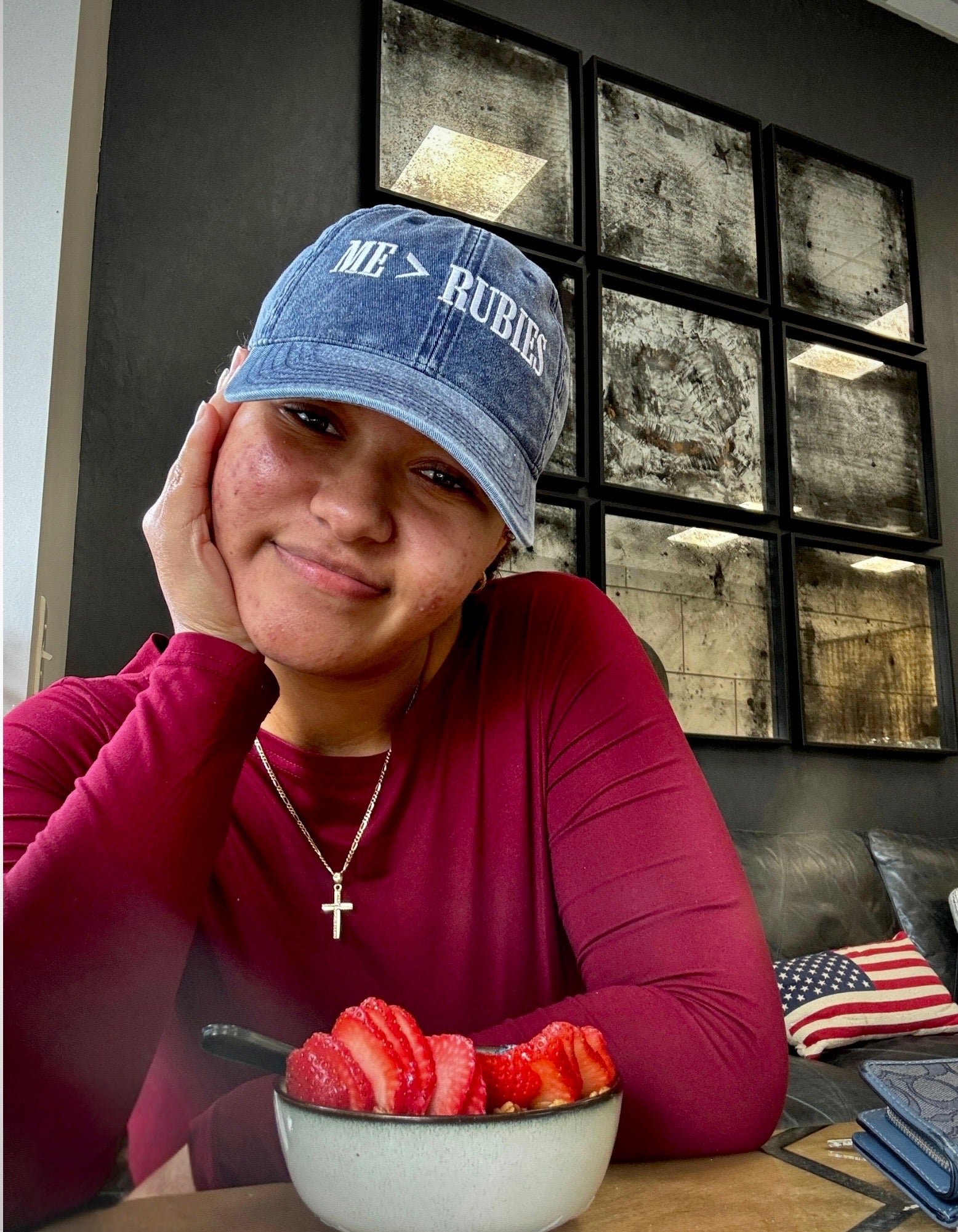 Person wearing a blue cap with text, sitting at a table with a bowl of fruit.