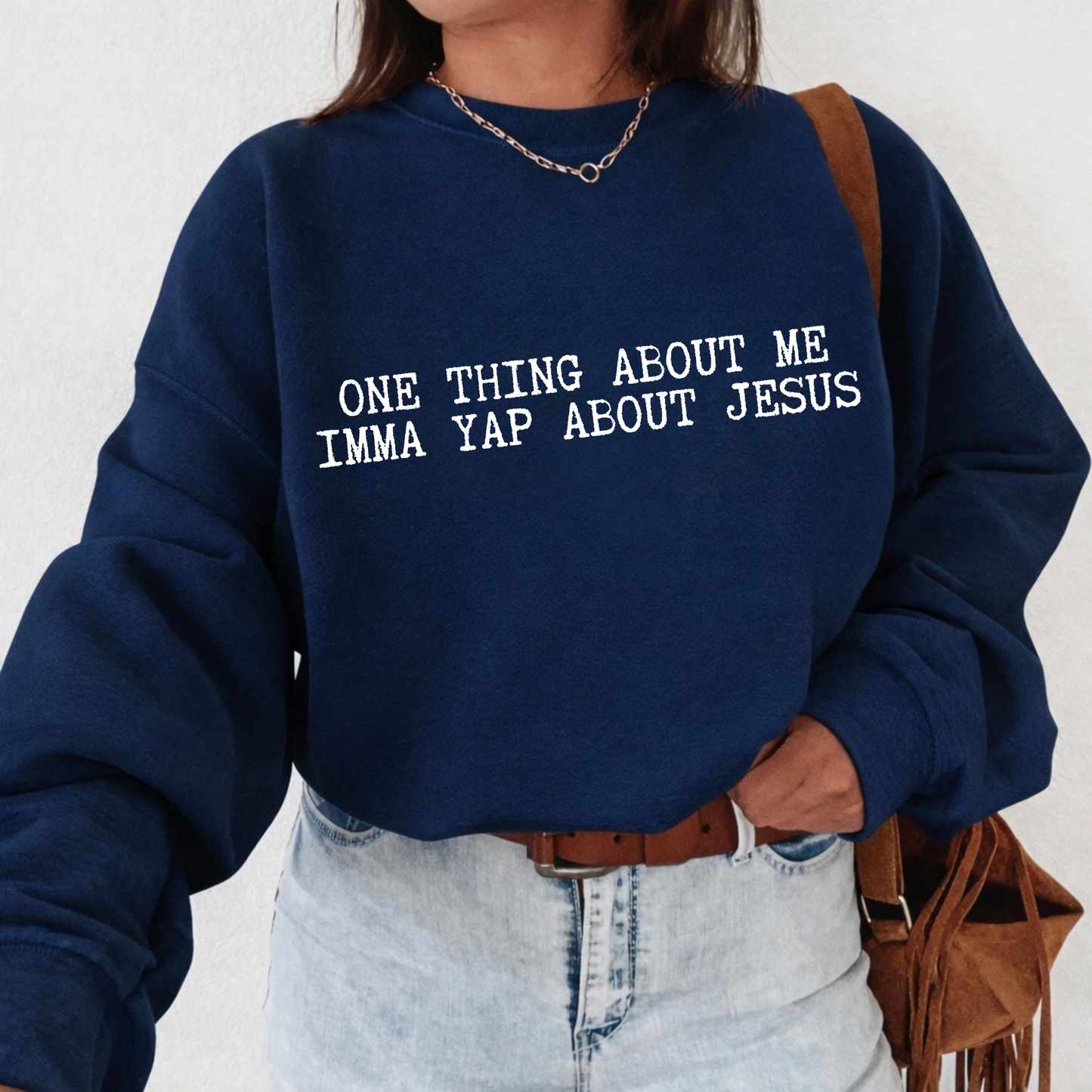 Person wearing a navy blue sweatshirt with text 'ONE THING ABOUT ME IMMA YAP ABOUT JESUS', standing against a white background