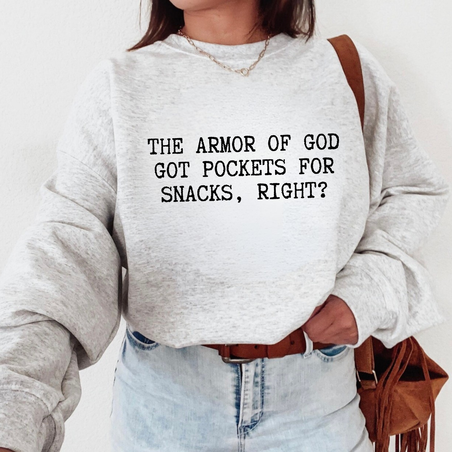 Person wearing a gray sweatshirt with text 'The Armor of God got pockets for snacks, right?' and holding a brown bag.