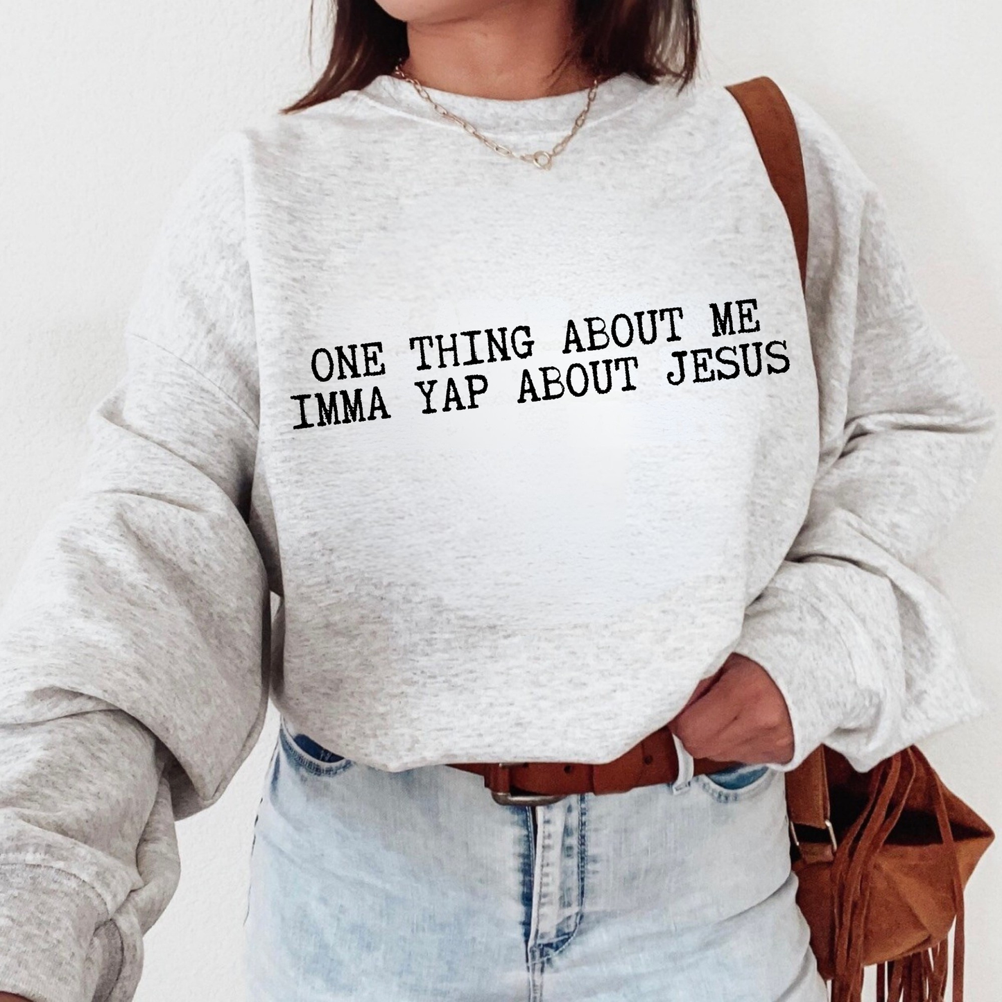 Person wearing a gray sweatshirt with text 'ONE THING ABOUT ME IMMA YAP ABOUT JESUS' on a plain background