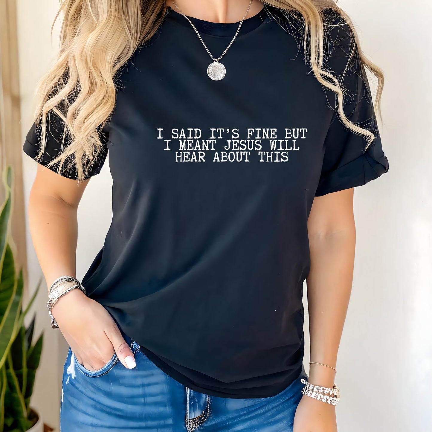 Person wearing a black t-shirt with humorous text "I said it's fine but I meant Jesus will hear about this" design.
