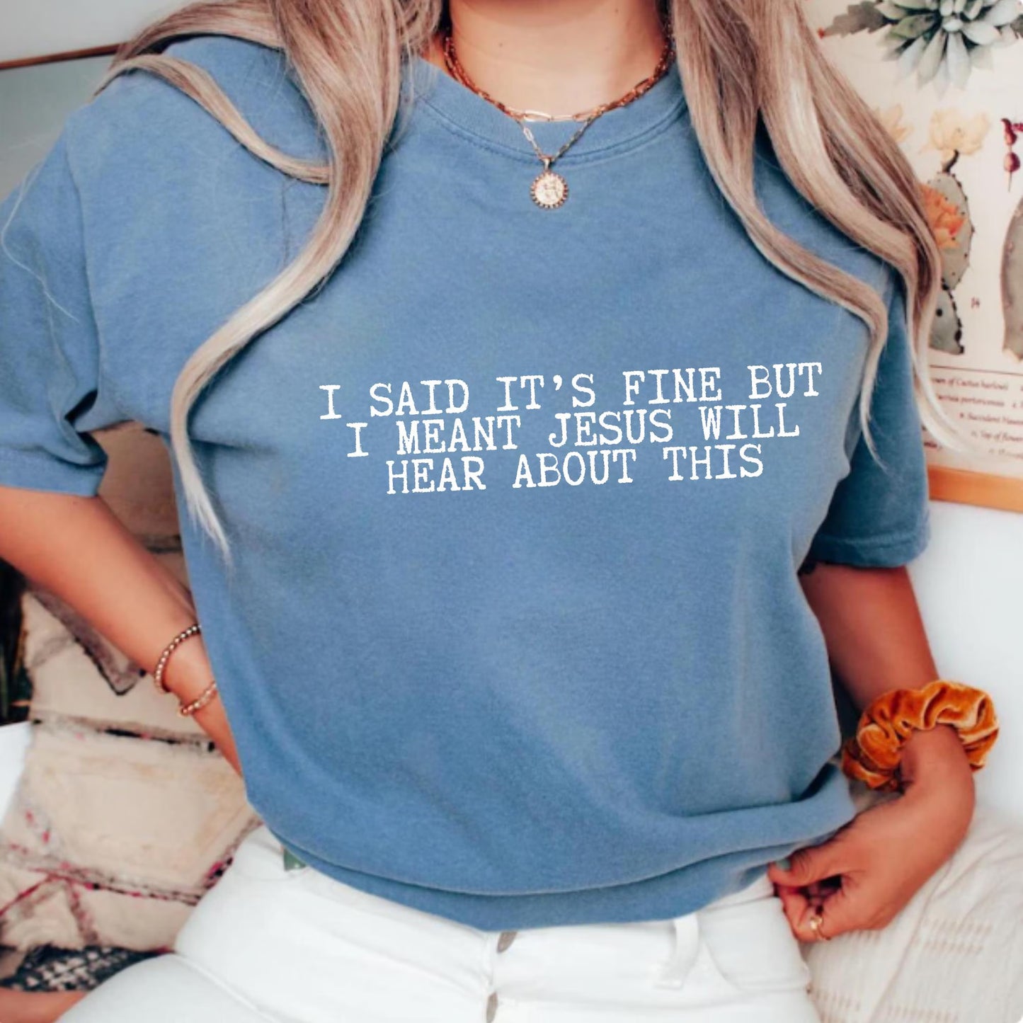 Person wearing a blue t-shirt with a humorous text "I said it's fine but I meant Jesus will hear about this" design.