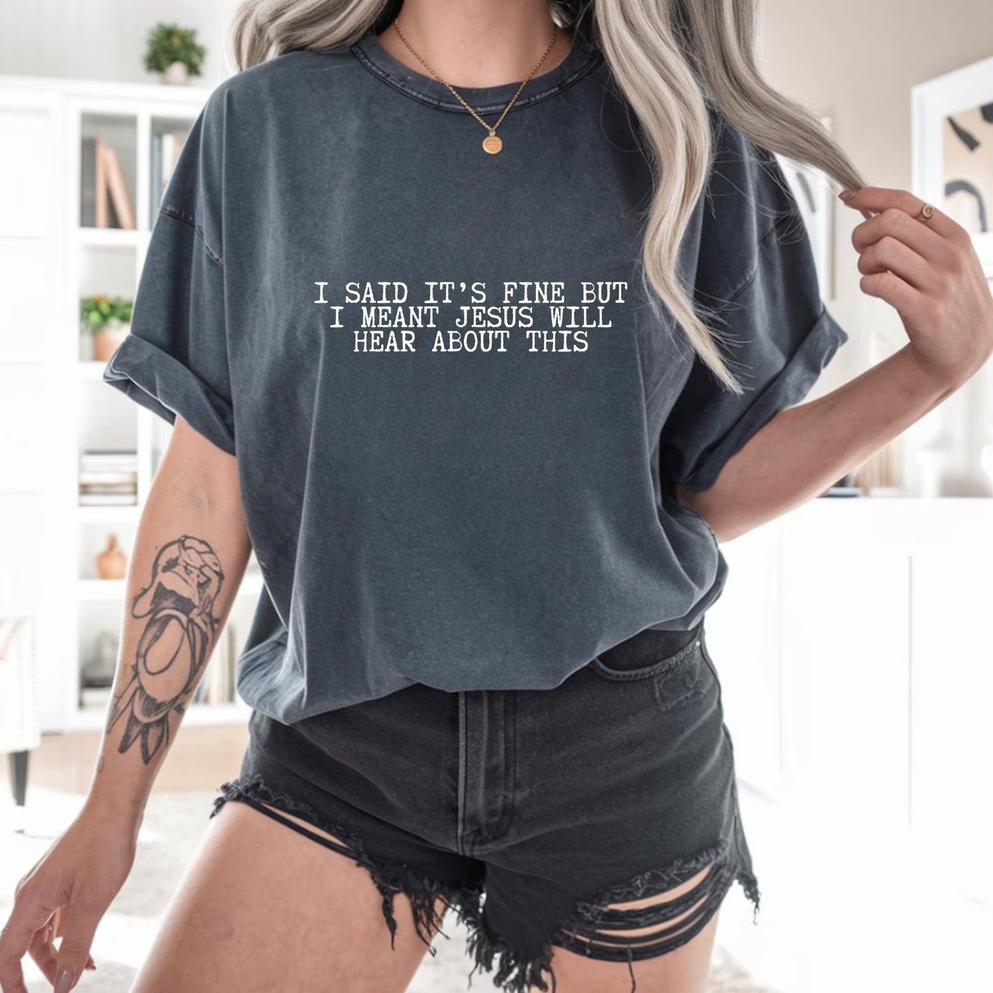 Person wearing a t-shirt with a humorous text "I said it's fine but I meant Jesus will hear about this" in a casual setting
