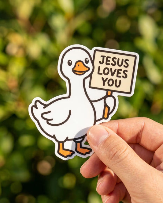 Sticker of a goose holding a 'Jesus Loves You' sign held by a hand with a blurred green background