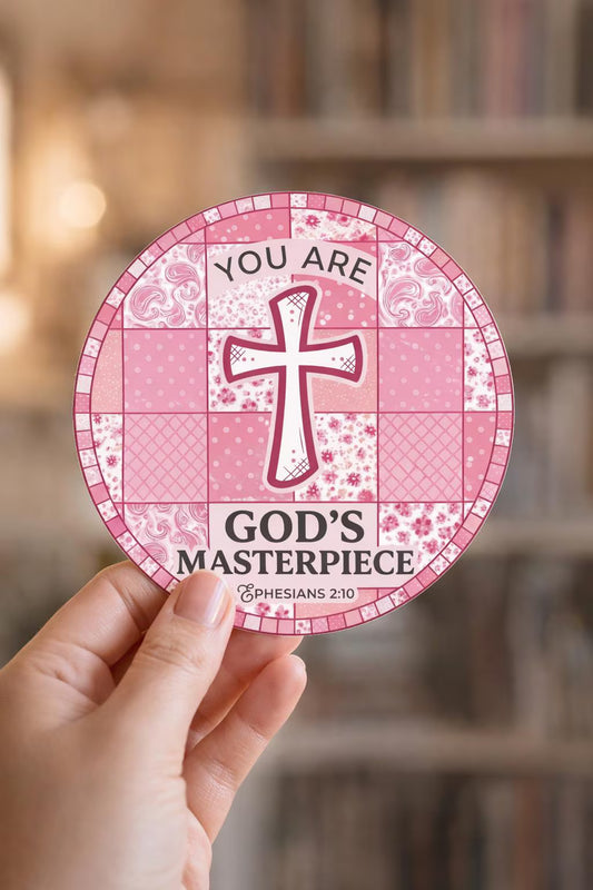 Pink circular sticker "You Are God's Masterpiece" with cross design held by a hand, blurred bookshelf in the background