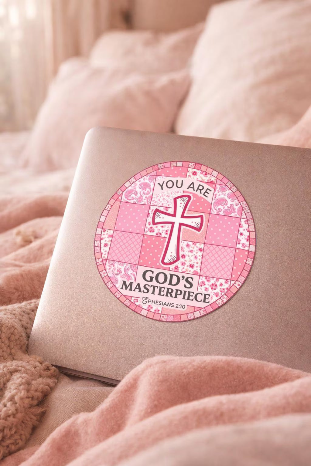 Pink laptop with a 'You are God's Masterpiece' sticker on a soft pink surface