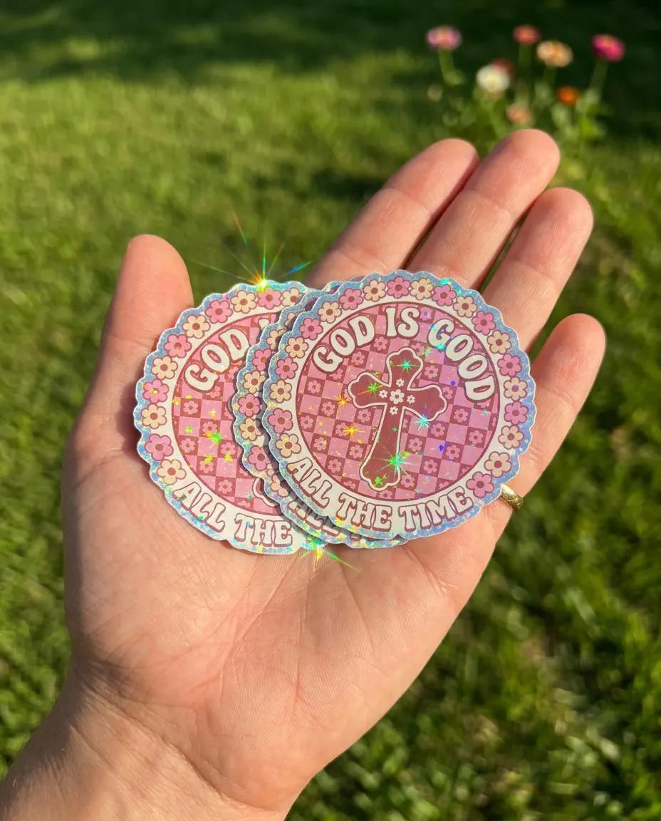 Set of holographic Christian stickers with pink floral checkerboard cross design and the phrase “God Is Good All The Time” in retro bubble lettering.